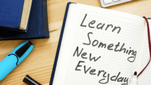 Open journaling notebook with handwritten reminder to "Learn Something New Everyday". Assorted books and highlighter surround the open notebook.