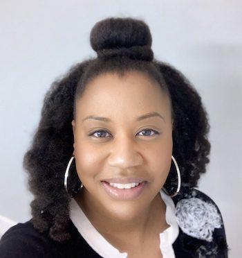 Professional headshot for Tasha Holmes. Tasha is a black woman with shoulder length hair, silver hoop earrings, wearing white and black blouse.