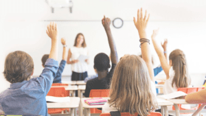 Image of teacher facing students with their hands raised ready to engage with her.
